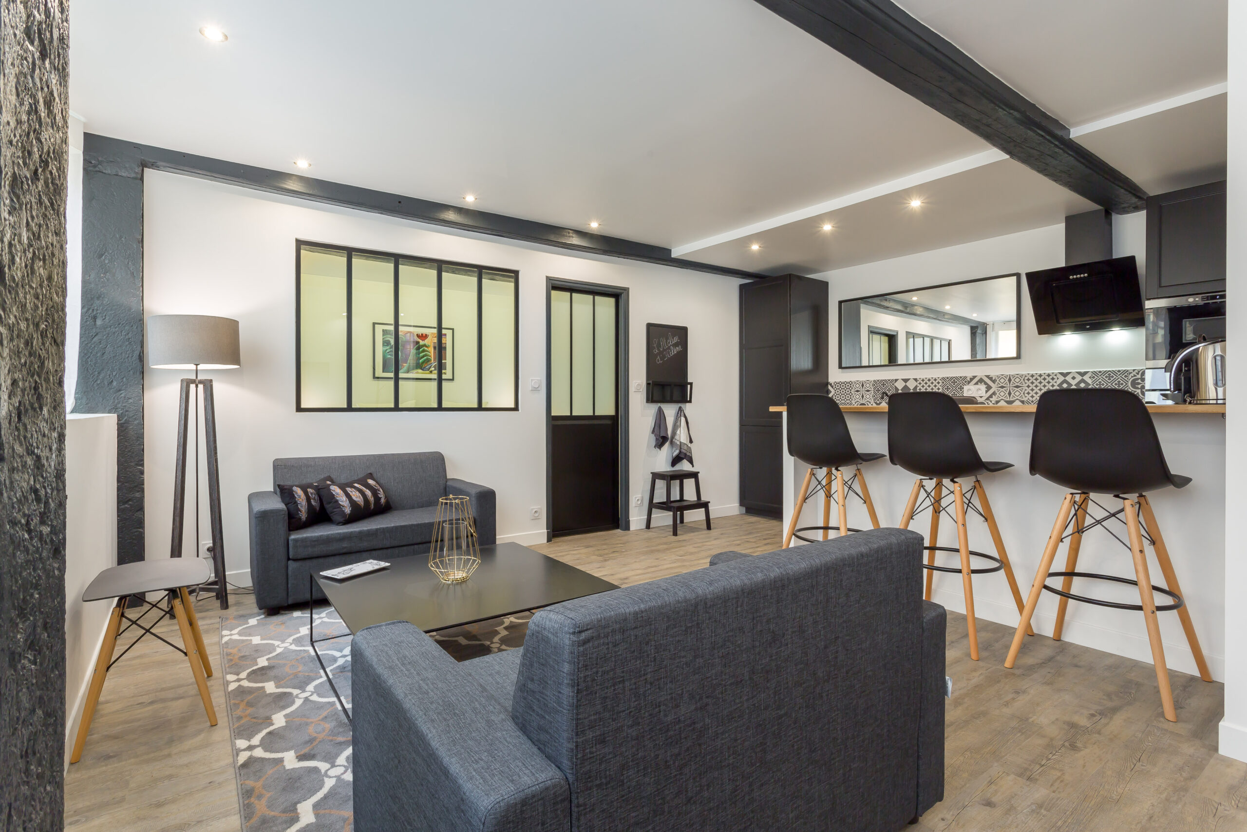 Atelier d’Hélène — Salon avec canapé sombre, fauteuil et verrière intérieure