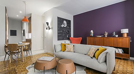 Un salon moderne avec un canapé gris, des coussins jaunes et gris, deux ottomans ronds tissés, un buffet en bois, une table de salle à manger ronde avec quatre chaises, et un mur d'accent violet avec des œuvres d'art monochromes. | 2BeApart Lyon