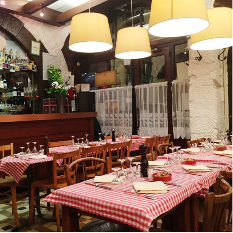 Restaurant confortable avec des tables en bois recouvertes de nappes à carreaux rouges et blancs, garnies de verres et de serviettes. Un éclairage chaleureux est suspendu au plafond, idéal pour les propriétaires exigeants à la recherche d'un lieu accueillant pour une moyenne durée. | 2BeApart Lyon
