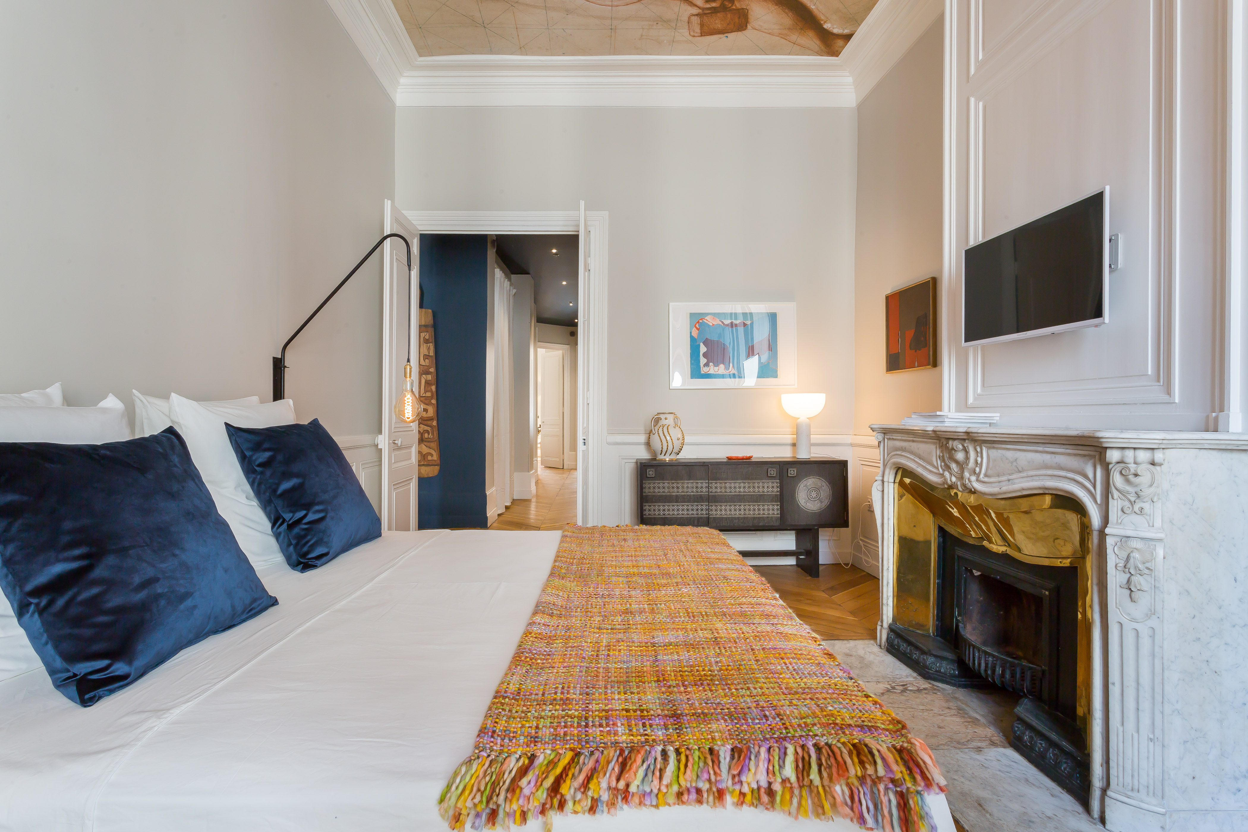 Chambre de l’appartement Blue Dream à Lyon, avec cheminée en marbre, coussins bleus et plafond peint.