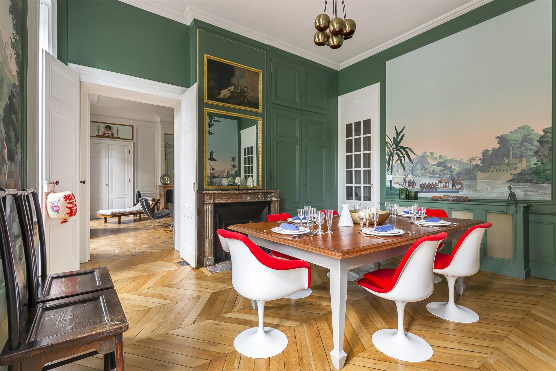 Salle à manger de l’appartement Tilsitt à Lyon, avec boiseries vertes, cheminée et chaises rouges et blanches.