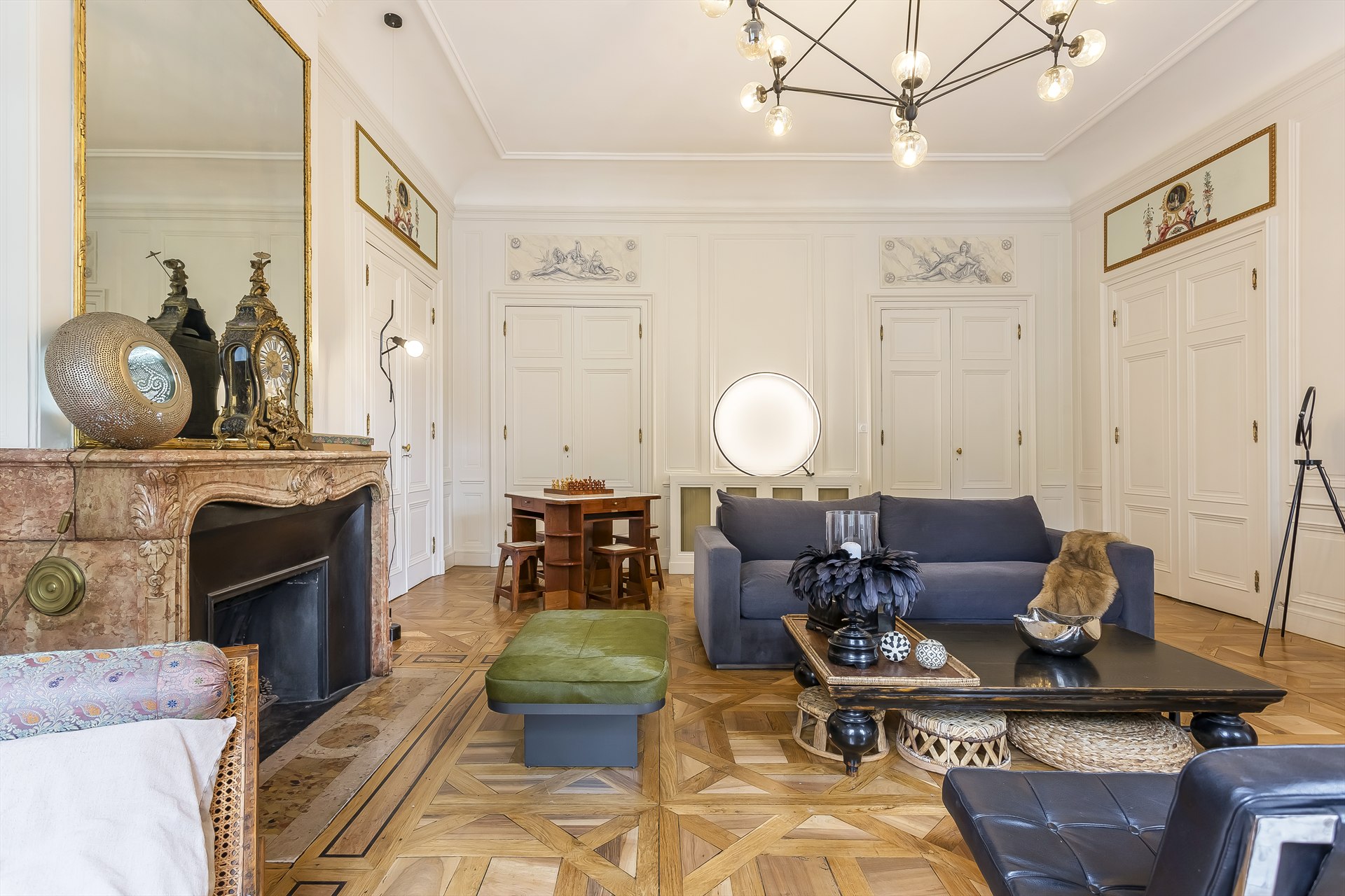 Salon de l’appartement Tilsitt à Lyon, avec cheminée en marbre, canapé bleu, pouf vert et parquet.