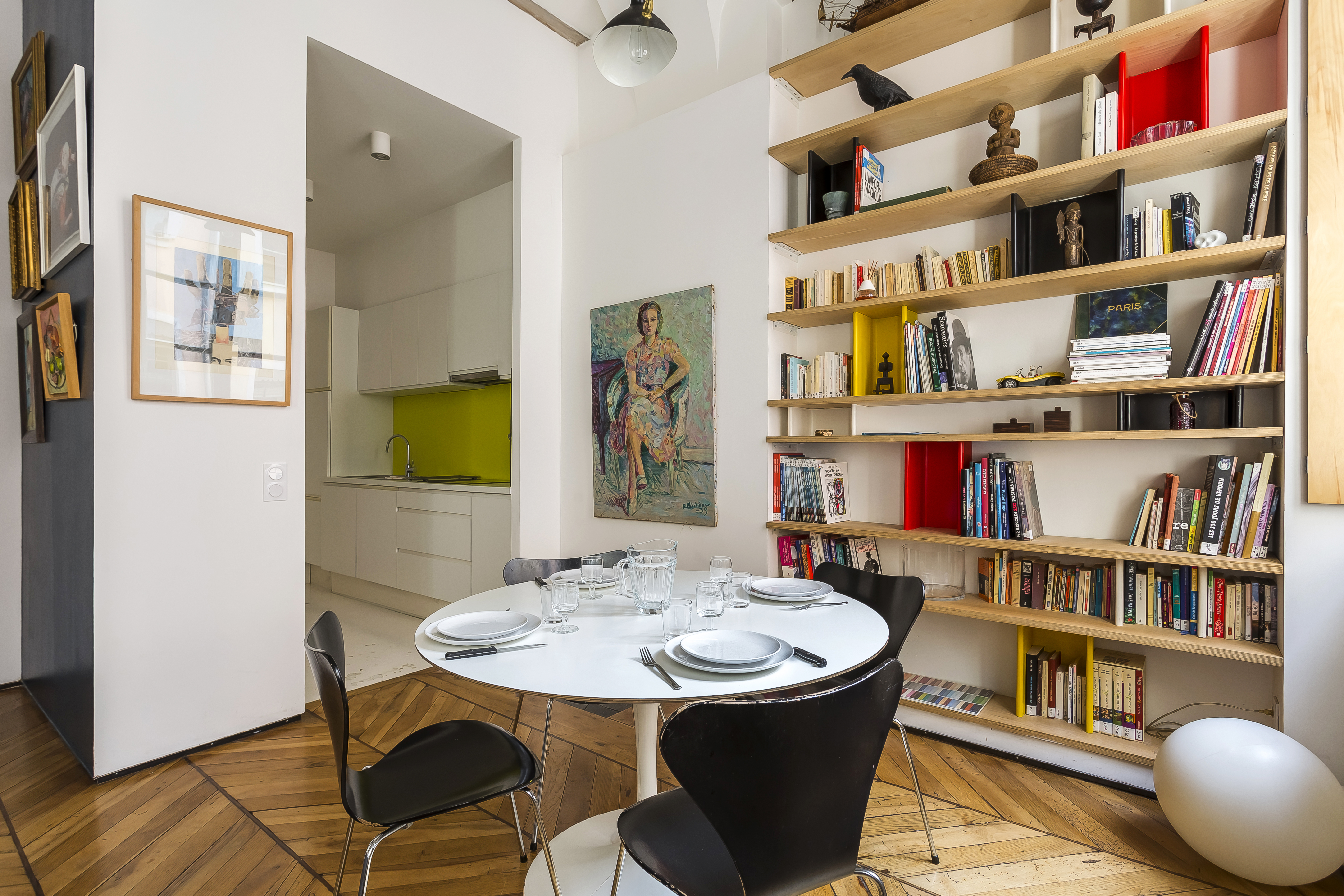 Espace repas de l’appartement Polycarpe, avec table ronde et grande bibliothèque.