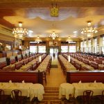 Un grand restaurant spacieux avec des rangées de tables garnies de nappes et de serviettes blanches, des cabines rouges, des lustres ornés, des colonnes de marbre et de grandes fenêtres inondant l'espace de lumière naturelle - parfait pour les propriétaires exigeants. | 2BeApart Lyon