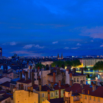 Un paysage urbain au crépuscule à Lyon révèle un mélange de bâtiments historiques et modernes sous un ciel bleu profond avec des nuages épars ; les lumières de la ville mettent en valeur les rues élégantes, idéales pour les propriétaires exigeants à la recherche d'une conciergerie haut de gamme. | 2BeApart Lyon