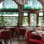 Restaurant élégant avec des tables rondes recouvertes de nappes blanches, des chaises en velours rouge, des vitraux et des murs en pierre voûtés. Parfait pour les propriétaires exigeants à la recherche d'une atmosphère raffinée ou pour ceux qui envisagent une localisation meublée Lyon pour moyenne durée. | 2BeApart Lyon